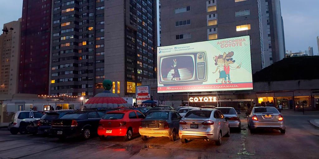 Un autocinema retro al atardecer, con coches clásicos y familias disfrutando de una película al aire libre.